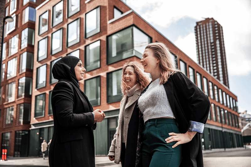 Tre kvinnor står utanför en byggnad och pratar